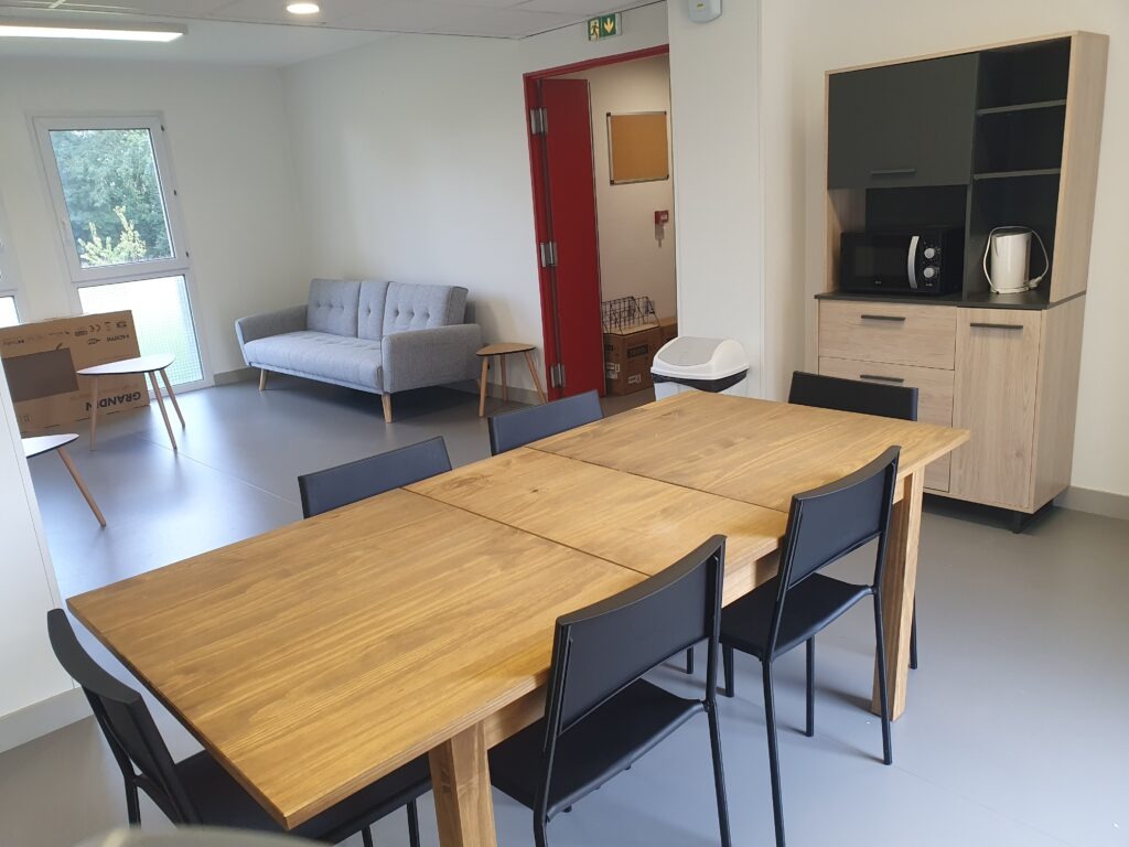 Espace de vie commun meublé avec table en bois, chaises noires, canapé et coin cuisine de la résidence étudiante du Campus Saint Aubin La Salle